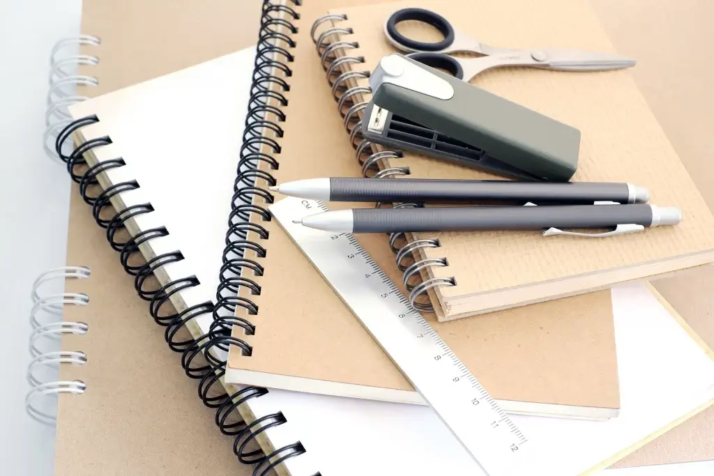 une pile de carnets avec une règle, deux stylos, une agrafeuse et une paire de ciseaux